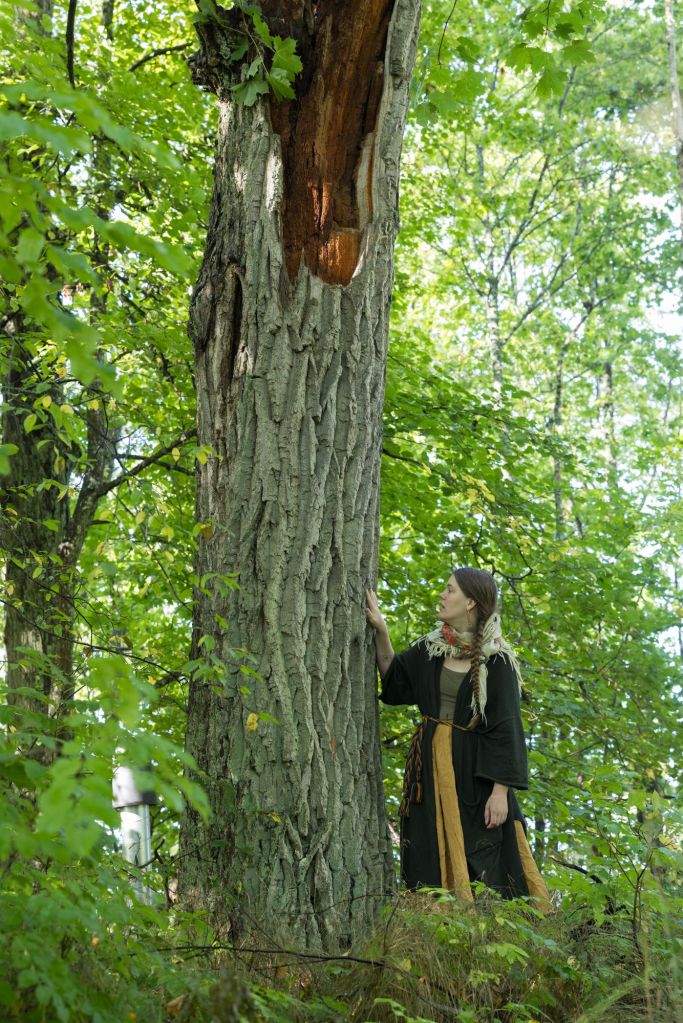 Inkeri Kurkilahti asuu luonnon äärellä ja koskettaa suurta puuta vihreässä metsässä.